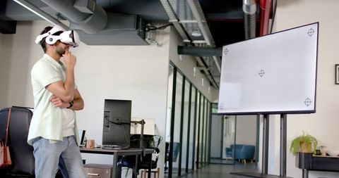 Indian man wearing vr headset evaluating large display in modern open-plan office