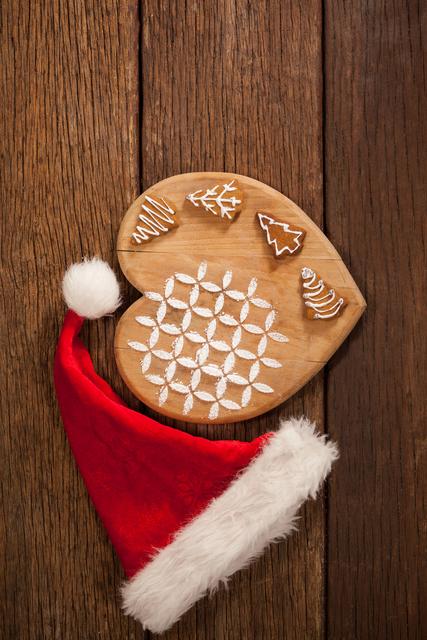 This image shows a wooden board with various gingerbread cookies decorated with icing, accompanied by a Santa hat. Ideal for holiday-themed promotions, Christmas recipes, festive greeting cards, and seasonal blog posts.