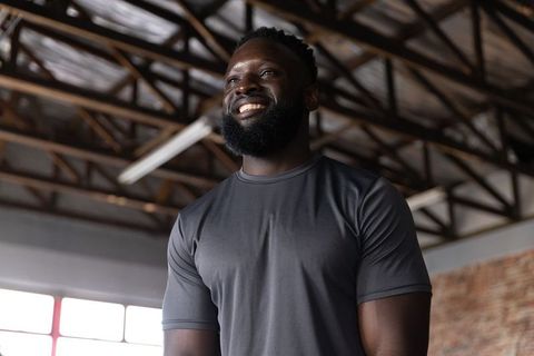 African american man smiling in gym loft wearing fitted tee, looking up inspired