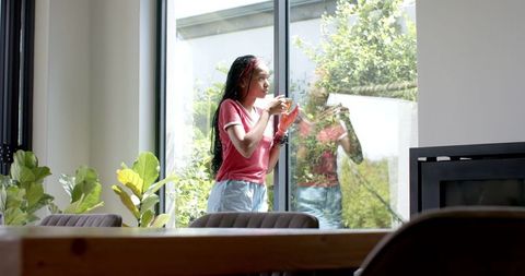 Young woman enjoying nature view indoors, holding beverage