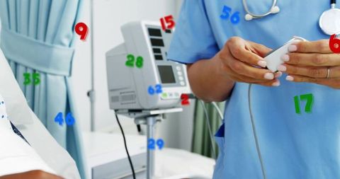 Mature nurse holding handheld monitor checking vital signs at bedside hospital ward