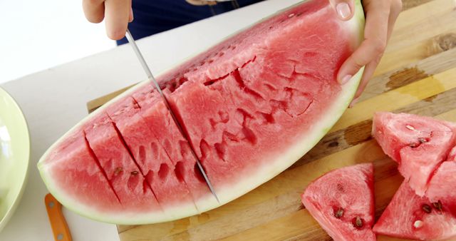 A person is slicing a ripe watermelon on a cutting board, with copy space. Fresh watermelon being cut indicates a preparation for a refreshing summer treat or a healthy snack.