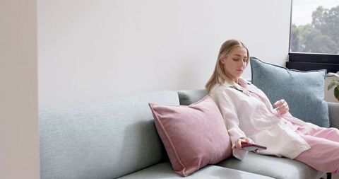 Pastel living relaxation: woman lounging on sofa in pale pink loungewear holding remote