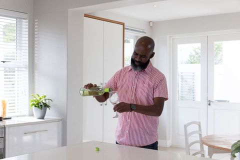 Mature man pouring white wine in stylish modern kitchen with potted plant