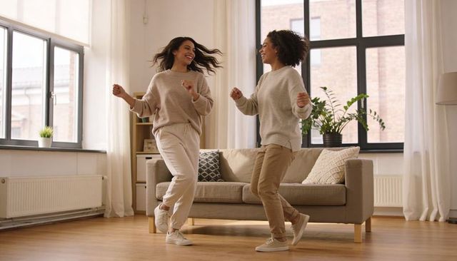 Dancing friends wearing neutral loungewear and sneakers in sunlit modern living room