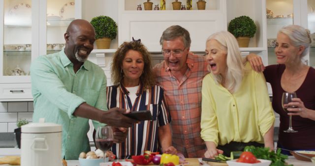 Image of happy diverse female and male senior friends preparing meal, using smartphone. retirement lifestyle, spending quality time with friends and technology.