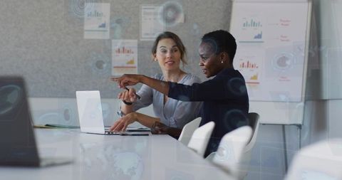 Collaborating and analyzing business data on laptop, pointing to charts in boardroom
