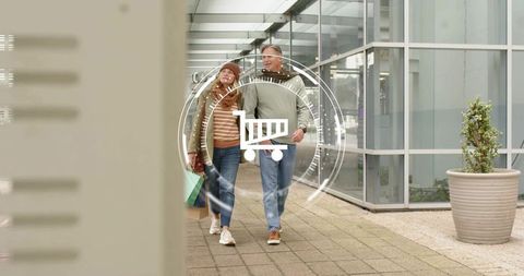 Mature couple walking with shopping bags through modern glass mall corridor with cart graphic