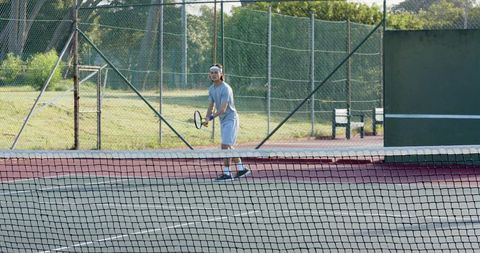 Asian tennis player holding racket behind net on outdoor court preparing to return serve
