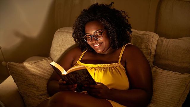 Cozy evening reading on sofa woman in yellow camisole wearing glasses enjoying paperback book