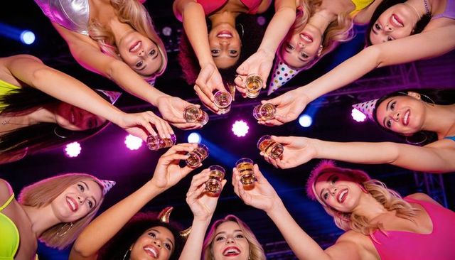 Women raising shot glasses in neon circle celebrating bachelorette party nightlife club vibe