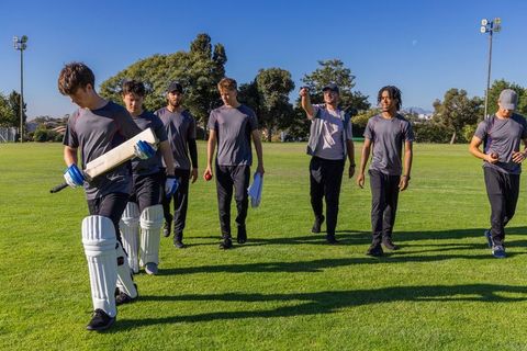 Young diverse cricket team walking on outfield carrying bats and pads after training