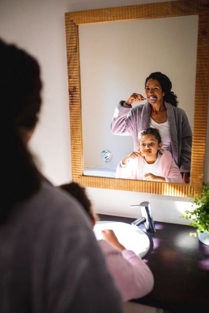 Mother and daughter enjoying a morning routine of brushing teeth together in the bathroom. The scene captures a moment of bonding and teaching good hygiene habits. Ideal for use in articles or advertisements related to family life, parenting tips, dental care, and healthy routines.