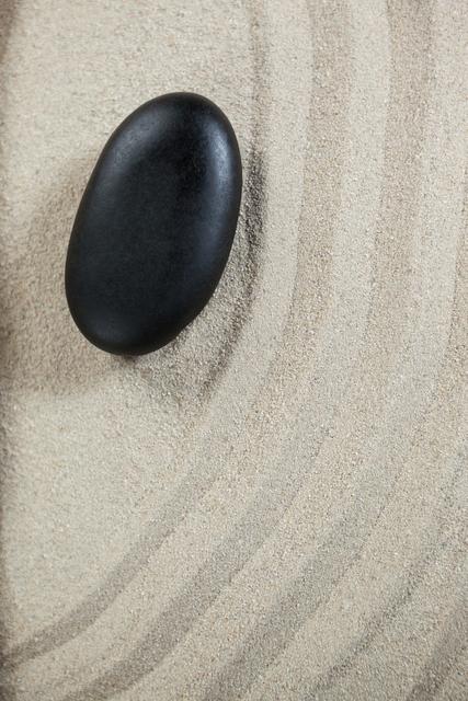 Black pebble stone resting on raked sand, evoking a sense of tranquility and balance. Ideal for use in wellness, meditation, and spa-related content. Perfect for illustrating concepts of simplicity, harmony, and natural beauty.