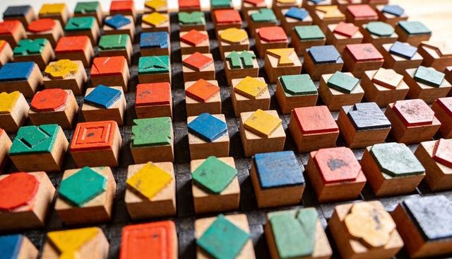 Worn colorful wooden shape blocks arranged in geometric grid on dark workshop tray