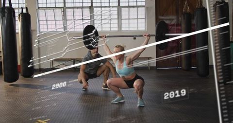 Female athlete performing overhead squat with trainer in industrial gym with data overlay
