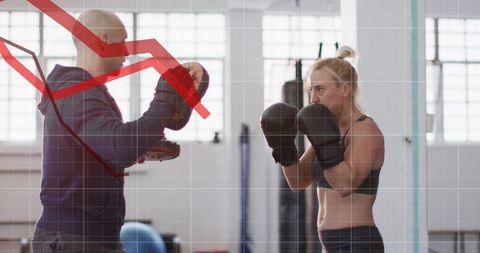 Female boxer sparring with coach holding pads in bright gym, red performance graph overlay
