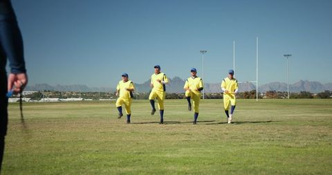 Male Teammates Running Drill in Yellow Kits and Blue Caps with Coach Timing Session