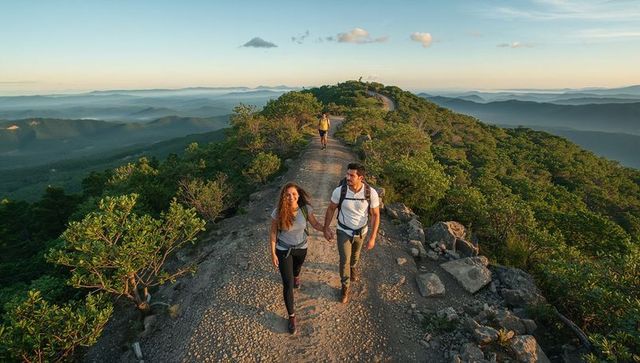 Hiking couple walking hand in hand along mountain ridge at sunrise with panoramic mountain views