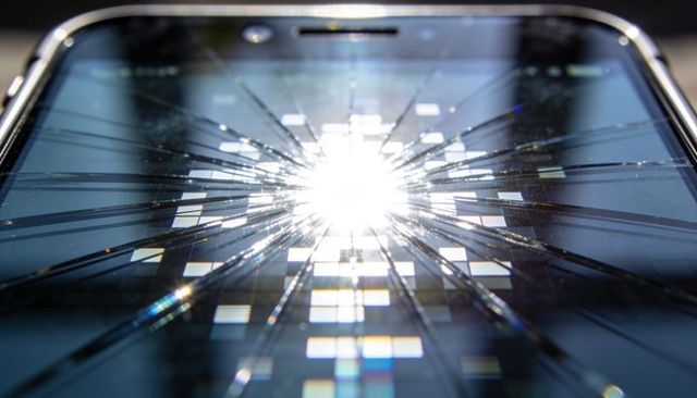 Shattered smartphone screen reflecting bright glare over pixel grid, macro crack detail