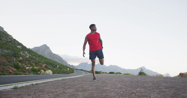 Man stretching before a morning run on a road surrounded by mountains. Ideal for fitness, health and wellness blogs, workout routines, and active lifestyle promotions. Scenic mountain background emphasizes the connection with nature.