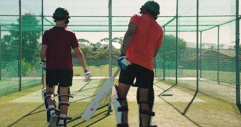 Diverse teammates entering cricket practice net tapping bats walking to wicket for batting drills