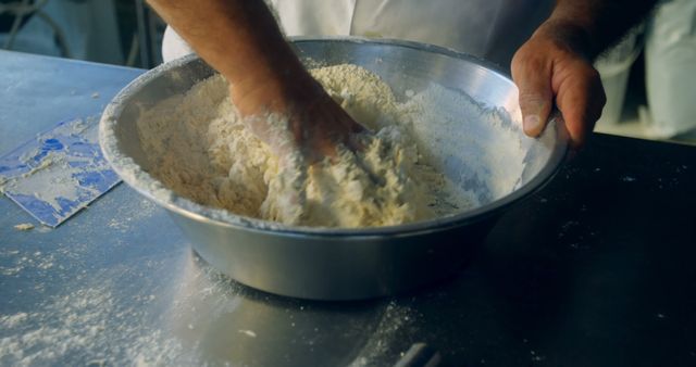 An overhead shot shows hands kneading dough in a large metal bowl in a kitchen. This image is perfect for illustrating food preparation, artisan baking, or culinary tutorials. Ideal for use in cooking blogs, recipe books, or advertisements for kitchen utensils and cooking classes.