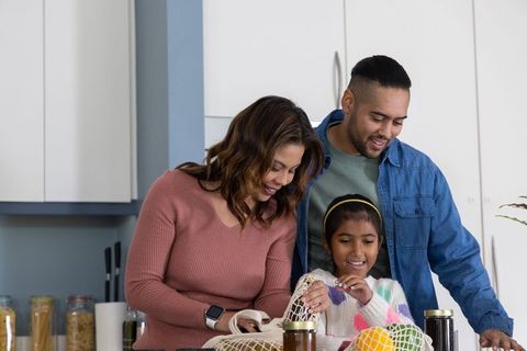 Family unpacking groceries at kitchen island using reusable mesh produce bags, smiling together