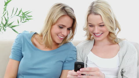 Two Friends Sharing a Text Message on Sofa in Bright Room