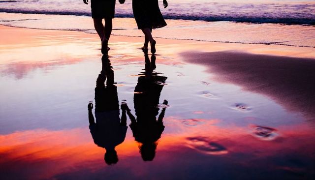 Romantic couple walking along reflective beach at colorful sunset leaving footprints at dusk