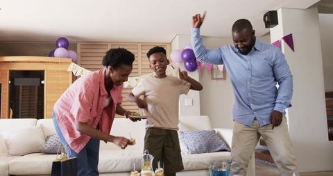 African American family celebrating birthday at home dancing and serving cupcakes with balloons