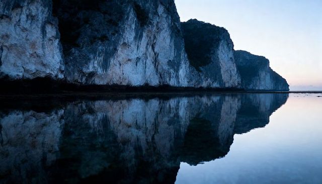 Mirroring limestone cliffs in glassy coastal tidal pool at dawn
