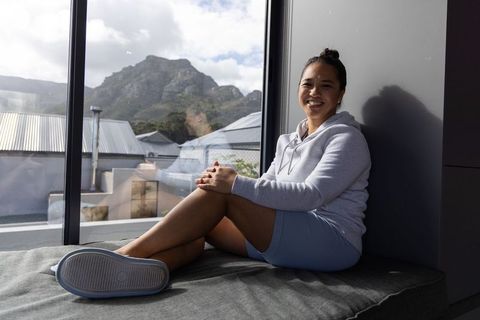 Asian woman sitting on window bench smiling in hoodie and shorts with mountain view