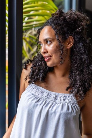 Sunlit african american woman smiling by metal window wearing white smocked strapless top