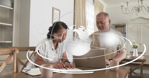 Senior couple reviewing finances and planning retirement at home with laptop and holographic globe