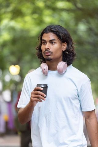 African american young man walking with coffee and pink headphones in urban park