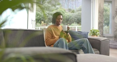 African American man sitting on sofa holding coffee mug in modern minimalist living room