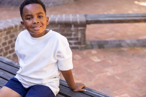 Smiling african american boy sitting on bench in sunlit urban brick plaza casual portrait