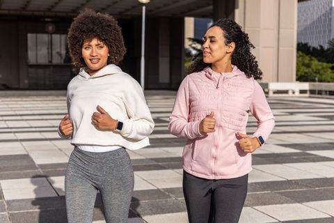 Urban friends jogging together wearing fitness watches on sunny tiled plaza