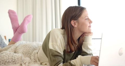 Woman Relaxing on Bed Using Laptop and Daydreaming Near Window