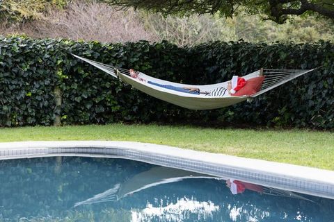 Middle-aged person relaxing in hammock by pool wearing santa hat and red cushion