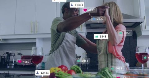Mature couple dancing while cooking at kitchen island with fresh produce and wine