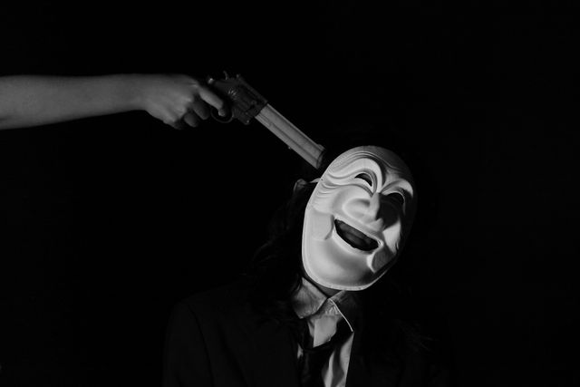 Masked person experiencing threat from a handgun, adding intense and dramatic ambiance. Can be used in articles or content discussing crime, fear, psychological themes, and mystery.