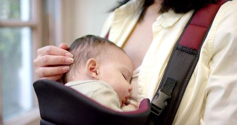 Mother comforting infant in home with baby carrier
