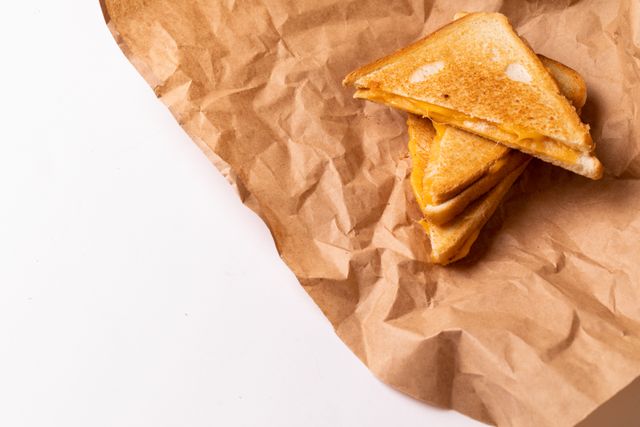 Grilled cheese sandwich placed on brown paper with white background, offering ample copy space. Ideal for food blogs, recipe websites, healthy eating promotions, and culinary magazines. Perfect for illustrating simple, homemade meals and comfort food.