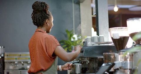 African american barista steaming milk at espresso machine in modern coffee shop counter