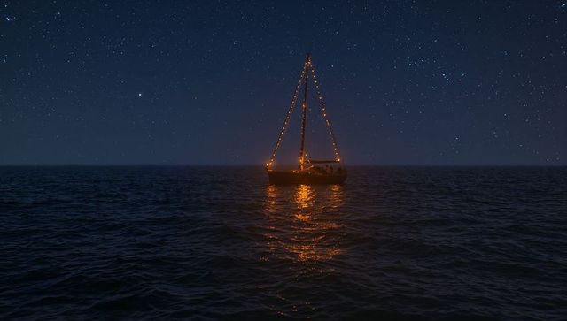 Drifting sailboat with glowing string lights under starry night sky reflecting on calm ocean