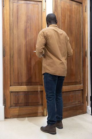 Man standing at tall paneled wooden double doors in narrow entry alcove holding smartphone