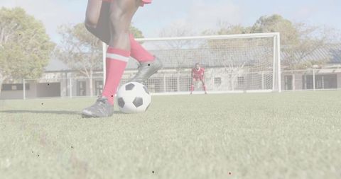 Soccer player controlling ball on turf near goal with goalkeeper bracing to save