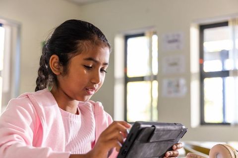 Indian schoolgirl using tablet in bright classroom concentrating on digital learning